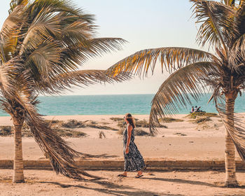 Rear view of woman standing at beach against sky