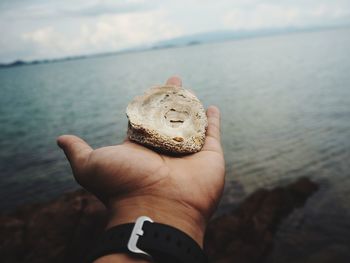 Close-up of hand holding rock at beach against sky