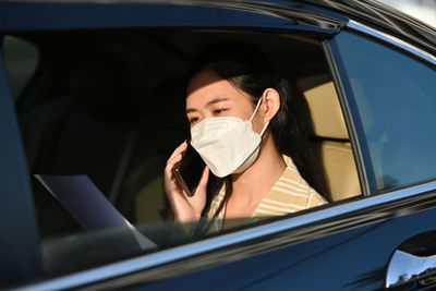 Businesswoman wearing mask talking on phone while sitting in car