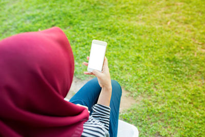 High angle view of woman wearing hijab using mobile phone while sitting in park