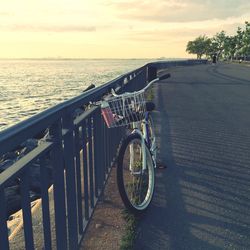 Bicycle on railing by sea against sky