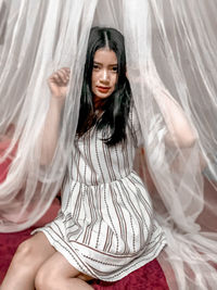 Portrait of a beautiful young woman sitting in curtain