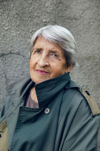 Portrait of an old grandmother of 90 with gray hair stands against a gray wall on the street