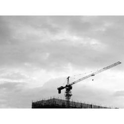 Low angle view of crane against cloudy sky