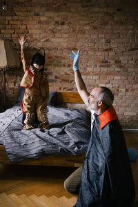 Father and son in superhero costumes playing in bedroom at home