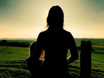 Rear view of woman standing on field during sunset