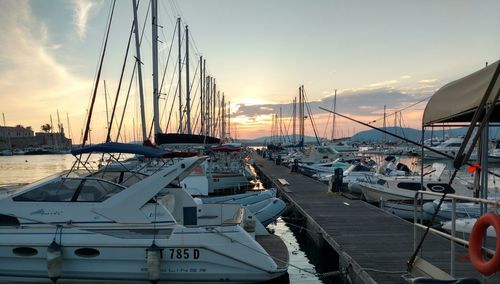 Boats moored in harbor at sunset