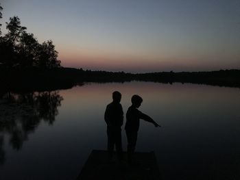 Silhouette men standing on lake against sky during sunset