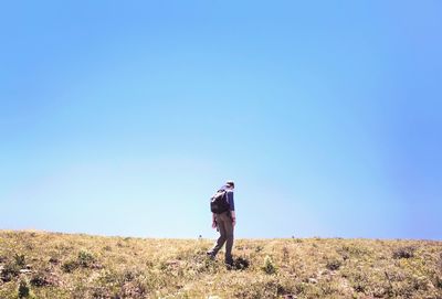 Rear view of man walking on field against clear blue sky