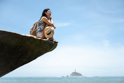 Beautiful asian girl sitting on a rock, enjoying the seaside in sunny summer's day