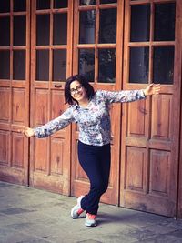 Portrait of happy young woman with arms outstretched by wooden doors