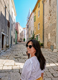 Young woman from behind, walking in city, looking back, old town, happy, smiling.