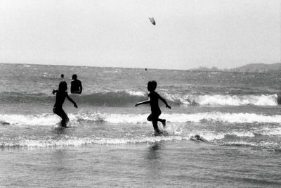 Silhouette children playing on beach against sky