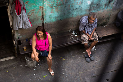 Full length of friends sitting on street against wall