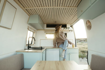 Contemplative woman with legs crossed sitting on kitchen counter inside motor home