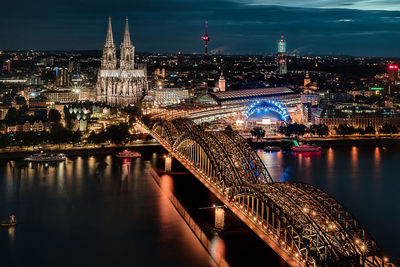 Illuminated bridge over river by cityscape at night