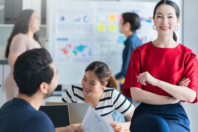 Portrait of smiling businesswoman with colleagues working in background