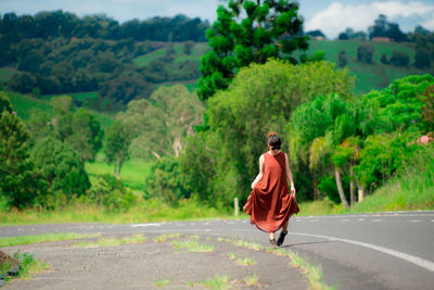 Young woman wearing sunglasses walking on road against trees in forest