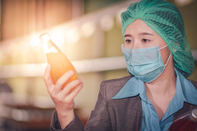 Close-up of woman wearing mask inspecting drink in factory