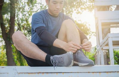 Man tying shoelace while sitting outdoors