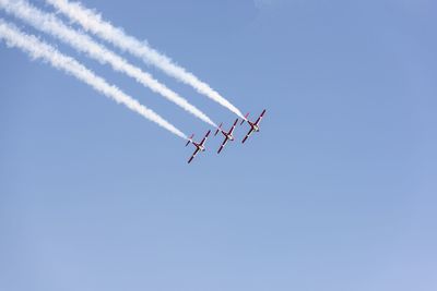 Low angle view of airshow against clear sky on sunny day
