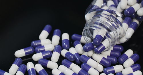 Close-up of pills spilling from bottle against black background