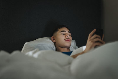 Teenage boy text messaging on smart phone while lying on bed in bedroom