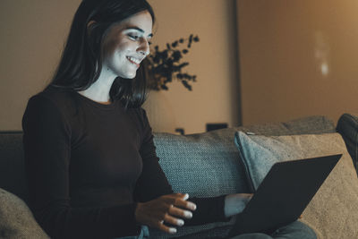 Young woman using laptop while sitting on sofa at home