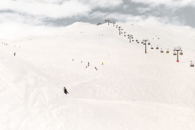 People skiing by ski lift on snowcapped mountains during sunny day