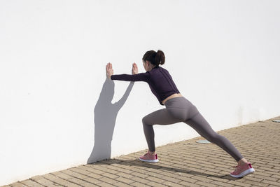 Sporty woman pushing against a white wall, warm up exercises.