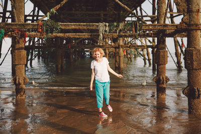 Full length portrait of smiling woman standing below eastbourne pier at beach