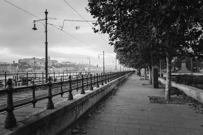 Footpath by street in city against sky