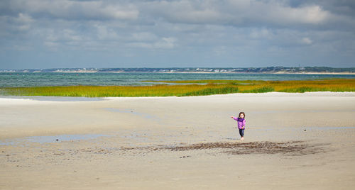 Small girl explores wide angle sandbar landscape with sea grass, sand, and blue sky