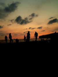 Silhouette people on beach against sky during sunset