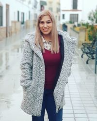 Portrait of smiling young woman wearing warm clothing standing in city during winter