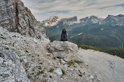 Rear view of woman sitting on rock against mountains and sky