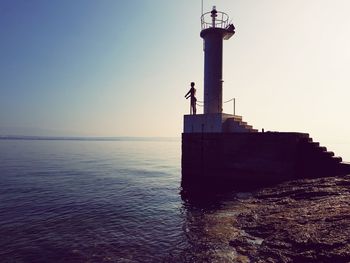 Lighthouse by sea against clear sky