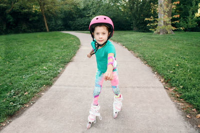 Girl in pink helmet riding in roller skates in park on summer day. seasonal outdoor activity sport