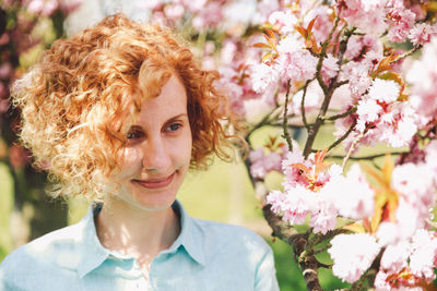 Close-up of smiling woman by blossoms on branch in park