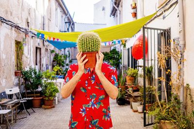 Full length of man holding a cactus plant against buildings in city