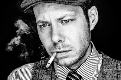 Close-up of thoughtful man smoking cigarette against black background