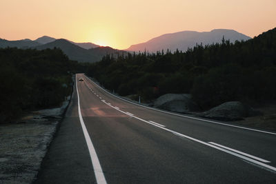Empty road leading towards mountains against sky during sunset
