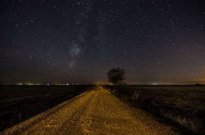 Dirt road amidst field against stars at night