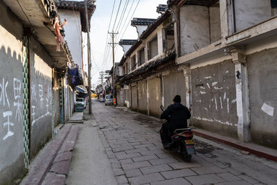 Rear view of man sitting on footpath amidst buildings