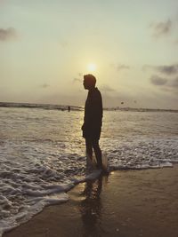 Man standing in sea against sky during sunset