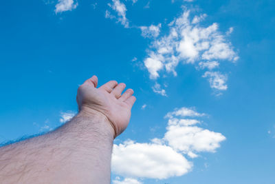 Cropped hand of man gesturing against blue sky