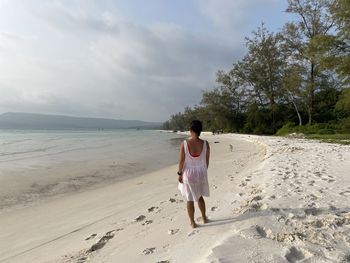 Rear view of woman standing at beach against sky