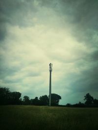 Low angle view of trees on grassy field against cloudy sky