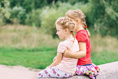 Two girls toddler sisters sit hugging on the bridge in the park. support.