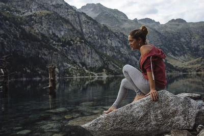 Woman with bun sitting on a rock by a lake during a trip.